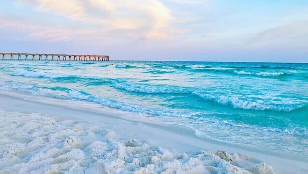 Ein Strand mit Wellen und einer Mole, die ins Wasser führt.