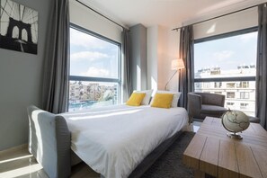 A hotel room with a large bed, a desk, and a view of the cityscape.