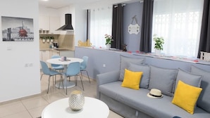 Ein modernes Wohnzimmer mit grauem Sofa, gelben Kissen, einem weißen Couchtisch und einem Essbereich mit blauen Stühlen.