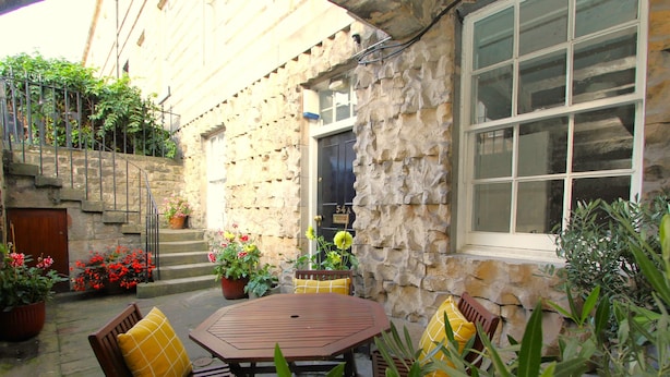 Une terrasse extérieure avec une table et des chaises en bois, entourée de plantes et de fleurs en pot.