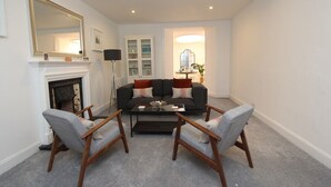 Un salon avec une cheminée, un canapé, deux fauteuils, une table basse et, au fond, un coin repas.
