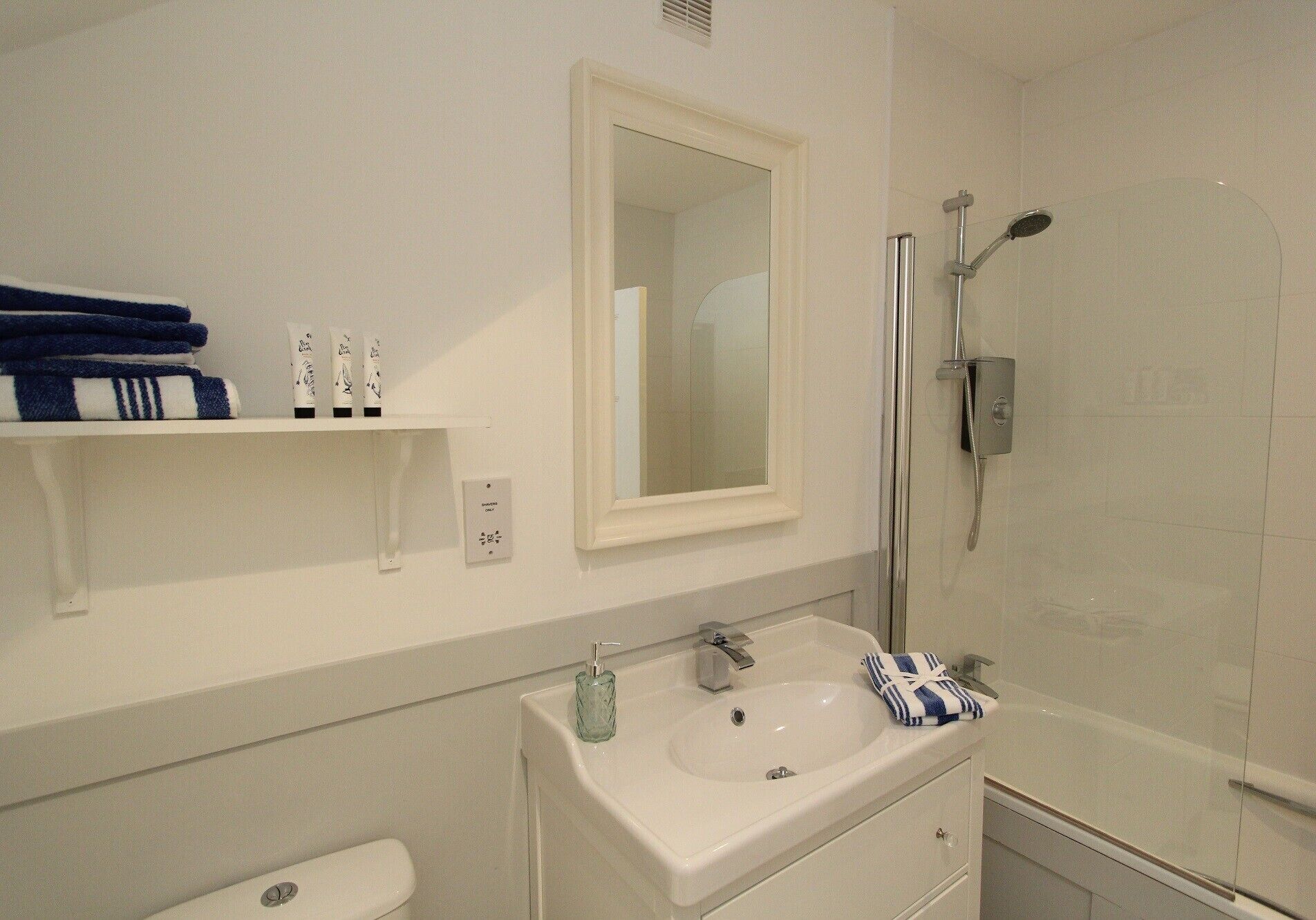 A bathroom with a white sink, a mirror, a shower, and a toilet. There are towels and toiletries on the sink.