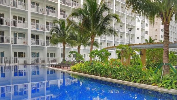 A hotel with a large indoor swimming pool surrounded by lush greenery and palm trees. - 1 BR Fully Furnished Condo Across MOA with Pool and Parking - Shore Bldg B, 1244 (Pasay City)