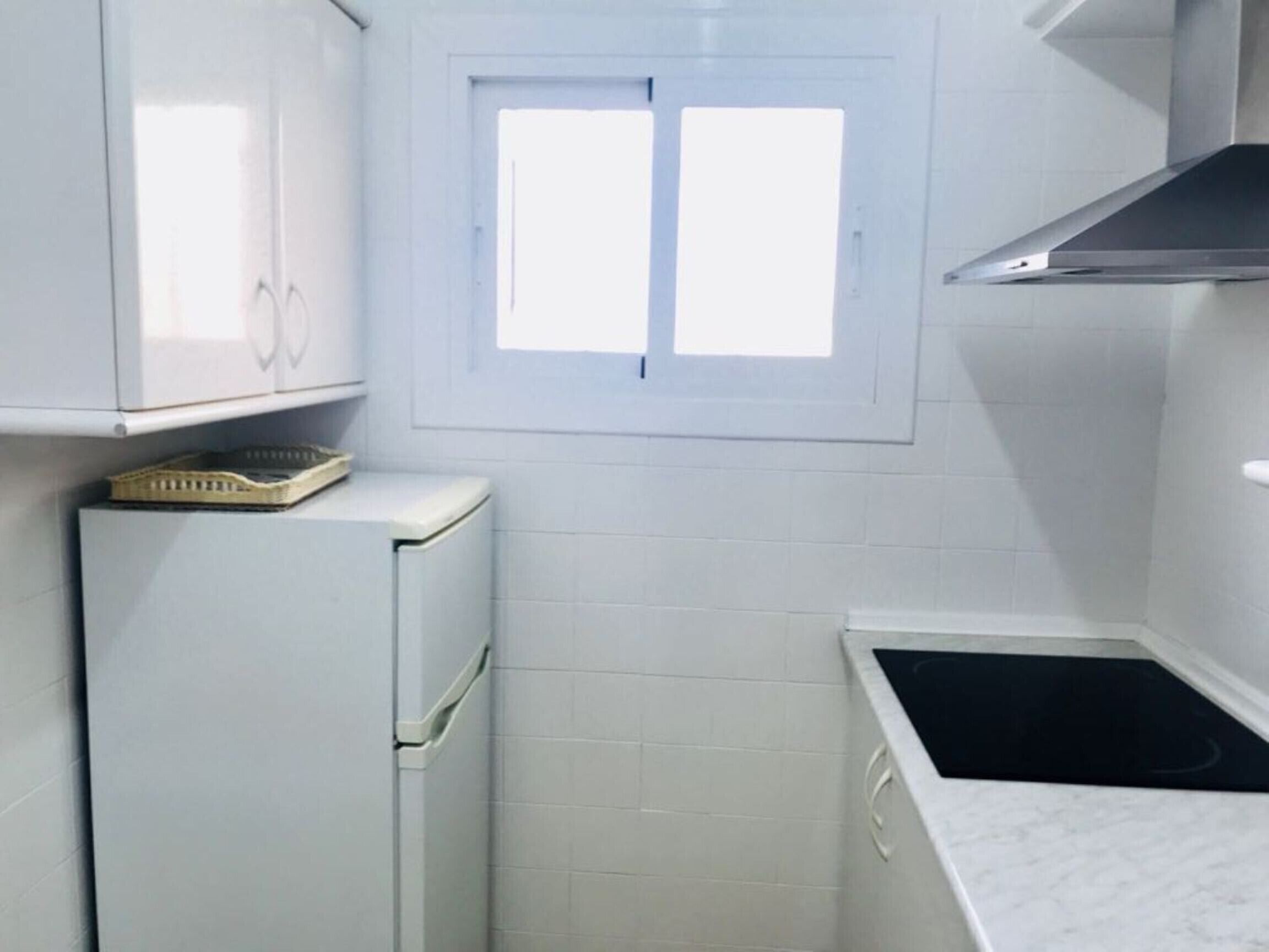 A compact kitchen with white cabinets, a small window, and a black sink.