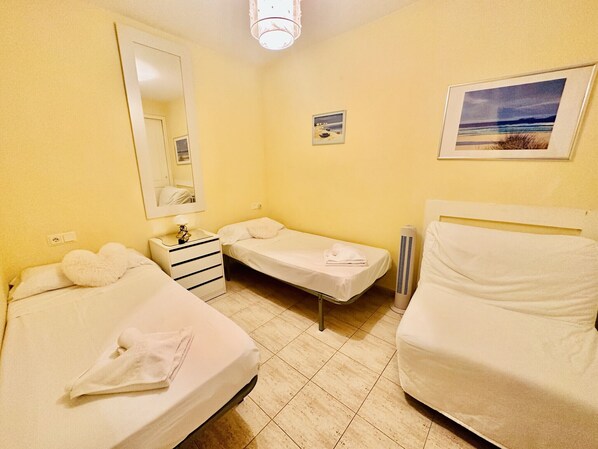 Habitación de hotel con dos camas individuales, una mesita de noche con lámpara, un espejo y un pequeño cuadro en la pared.