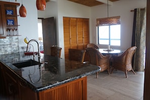 Una cocina con encimera de granito, armarios de madera y un comedor con sillas de mimbre.