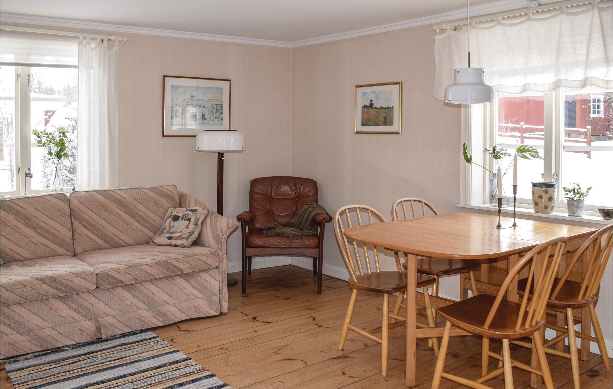 A living room with a sofa, a chair, a dining table with chairs, two framed pictures on the wall, and a floor lamp.