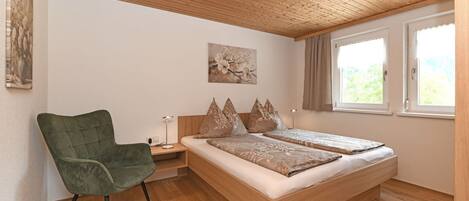 A bedroom with a wooden ceiling, a bed with pillows, a chair, and a nightstand.