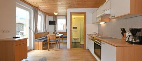A compact kitchen with wooden cabinets, a dining area with a bench, and a visible bathroom.