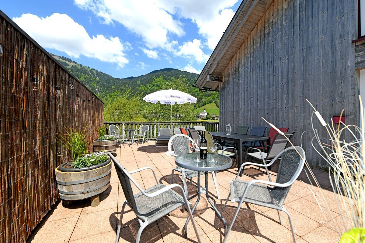 An outdoor patio with metal chairs and tables, a wooden fence, and a view of a mountain.
