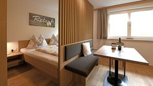 Una habitación con cama, un banco, una mesa y una ventana.