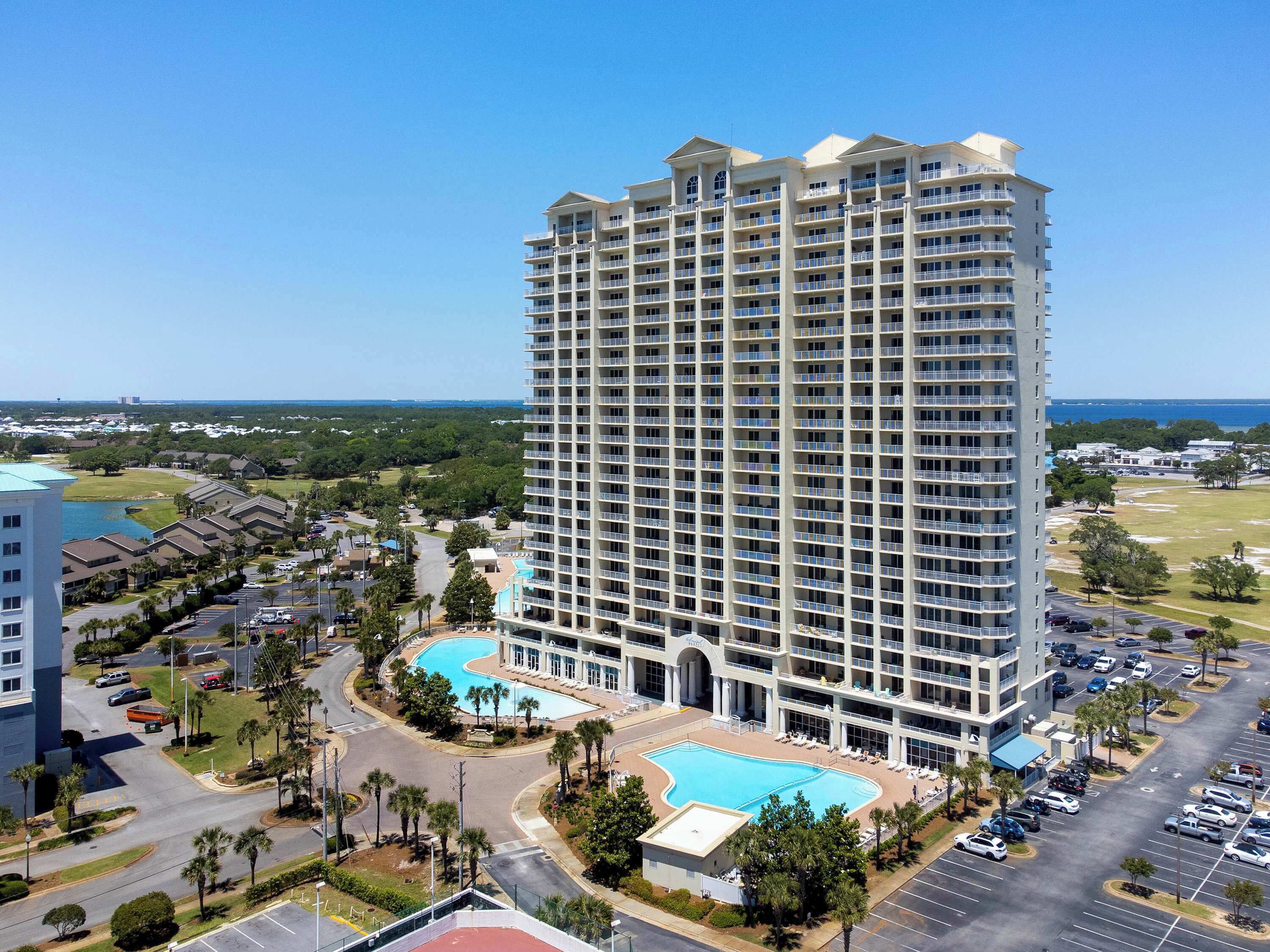 A high-rise hotel with multiple balconies, a swimming pool, and a parking lot.