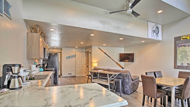 A modern kitchen with marble countertops, a coffee machine, and a dining area with a wooden table and leather chairs. - Charming Home - 1 Mi to Yellowstone National Park! (West Yellowstone)
