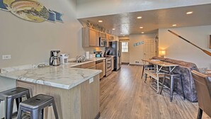 A modern kitchen with a marble countertop, wooden cabinets, and a built-in island with bar stools. - Charming Home - 1 Mi to Yellowstone National Park! (West Yellowstone)