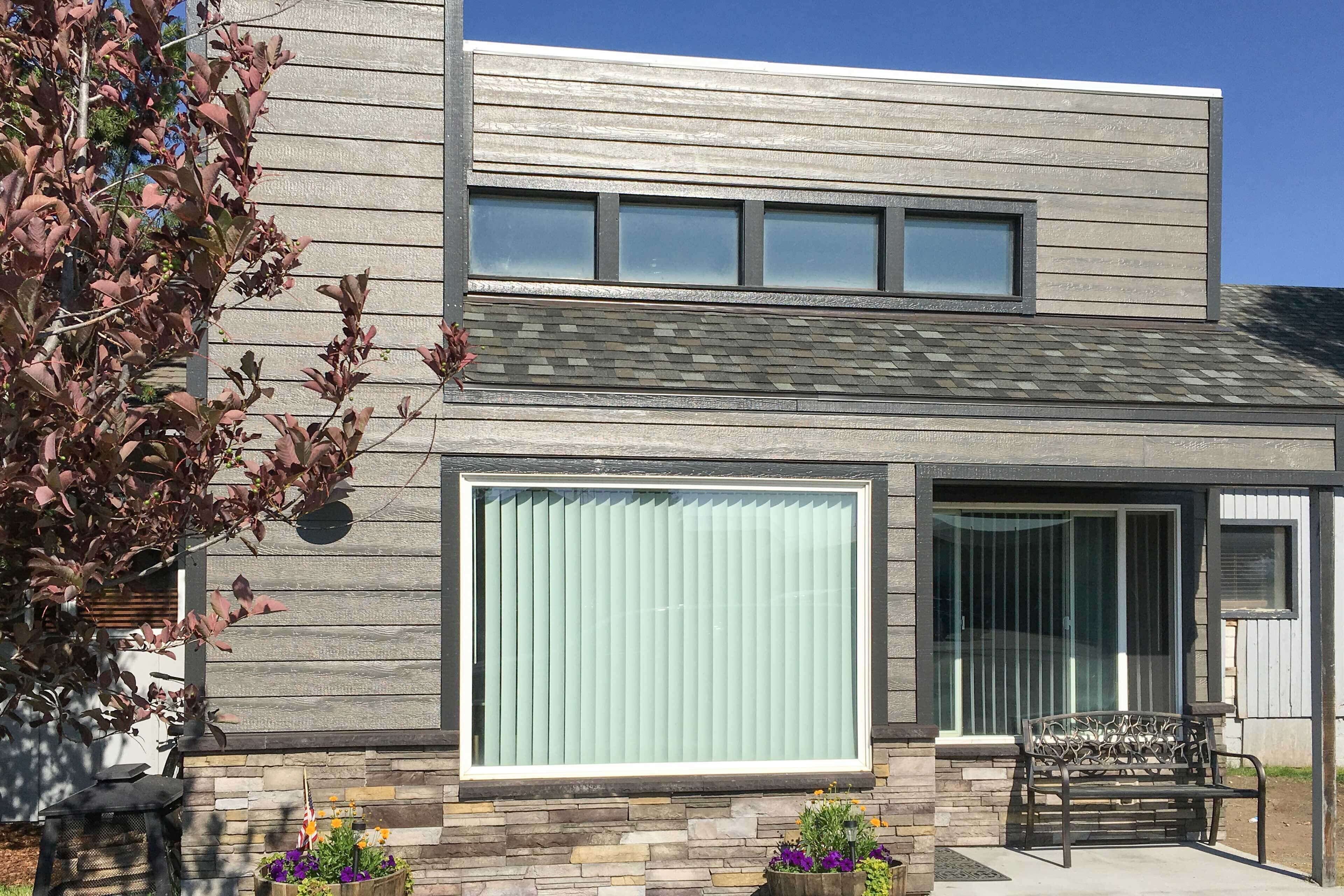 A modern two-story house with a stone facade, large sliding glass doors, and a patio with a bench.