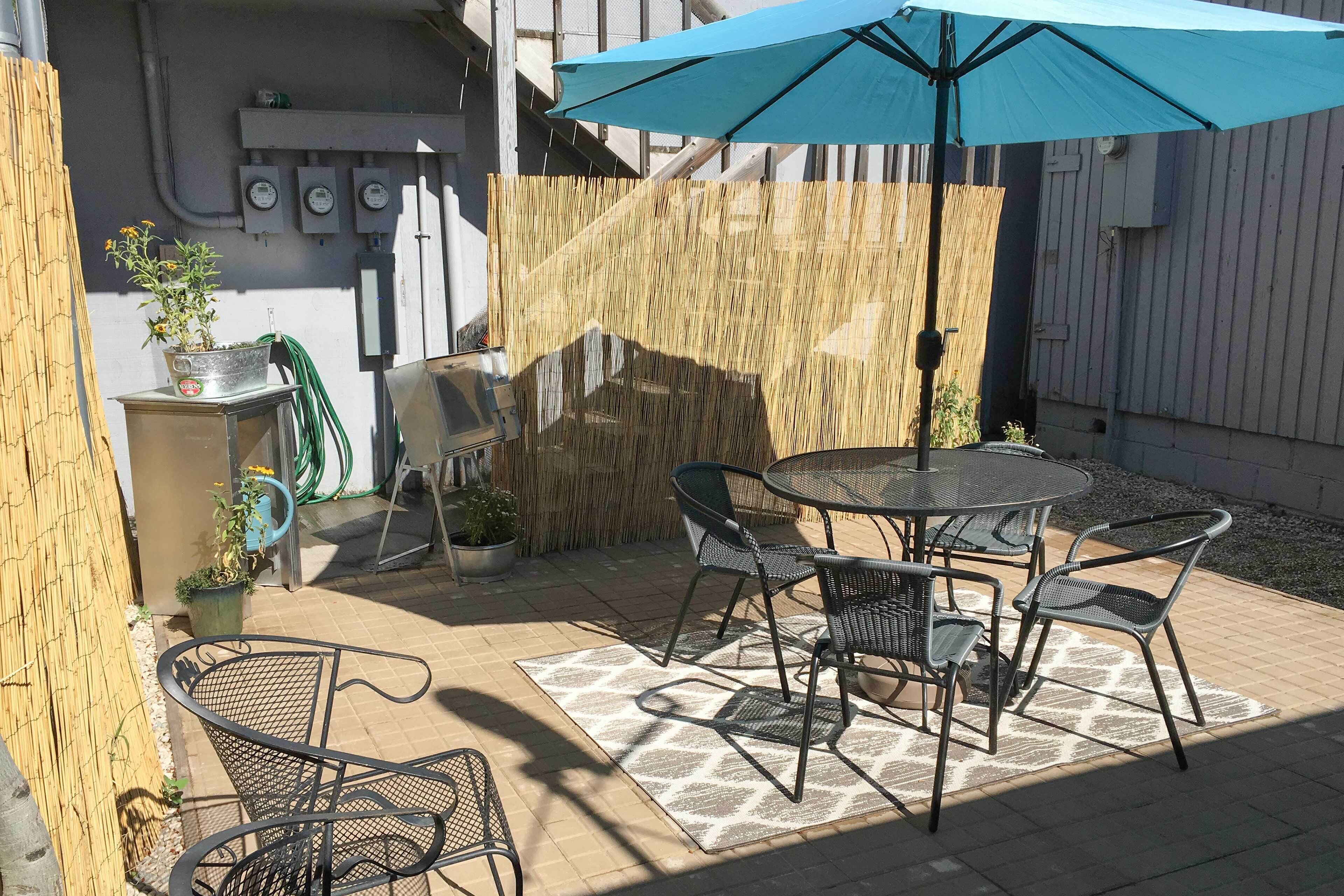 Une terrasse extérieure avec une table ronde et des chaises, un parasol bleu et des plantes en pot.