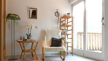 Een kamer met een stoel, een tafel met een plant, een boekenkast en een raam met uitzicht.