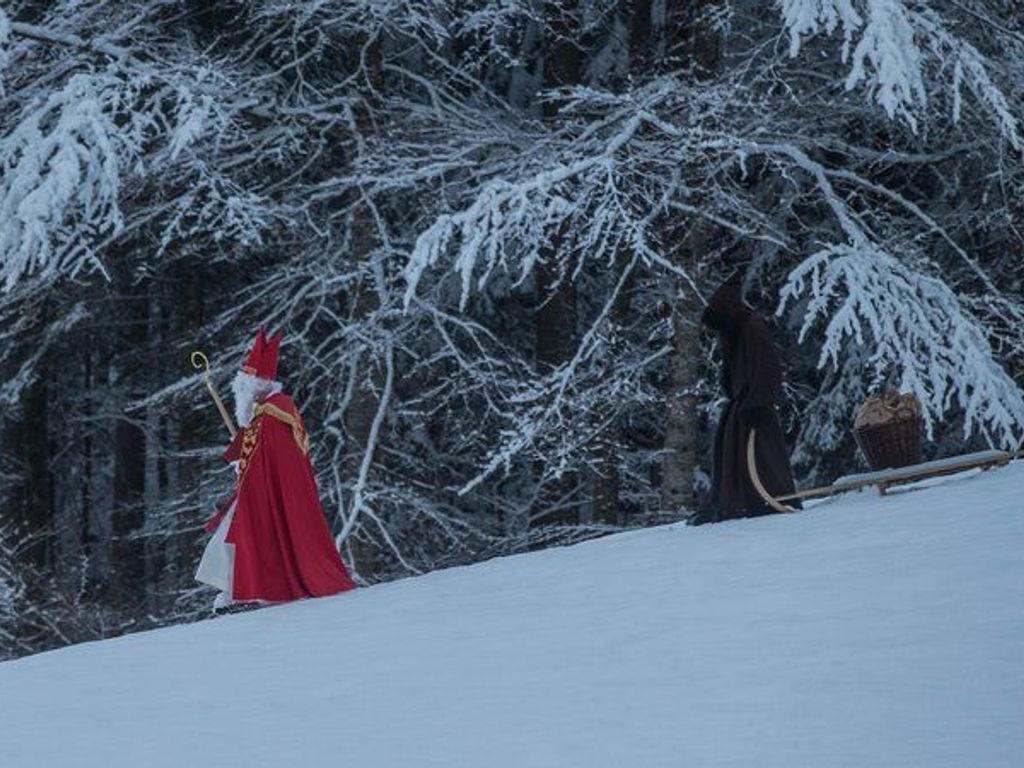 A person in a red robe walking on a snow-covered slope with trees in the background.