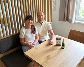 A room with a wooden slatted wall, a wooden table with a bottle of champagne, and a bench.