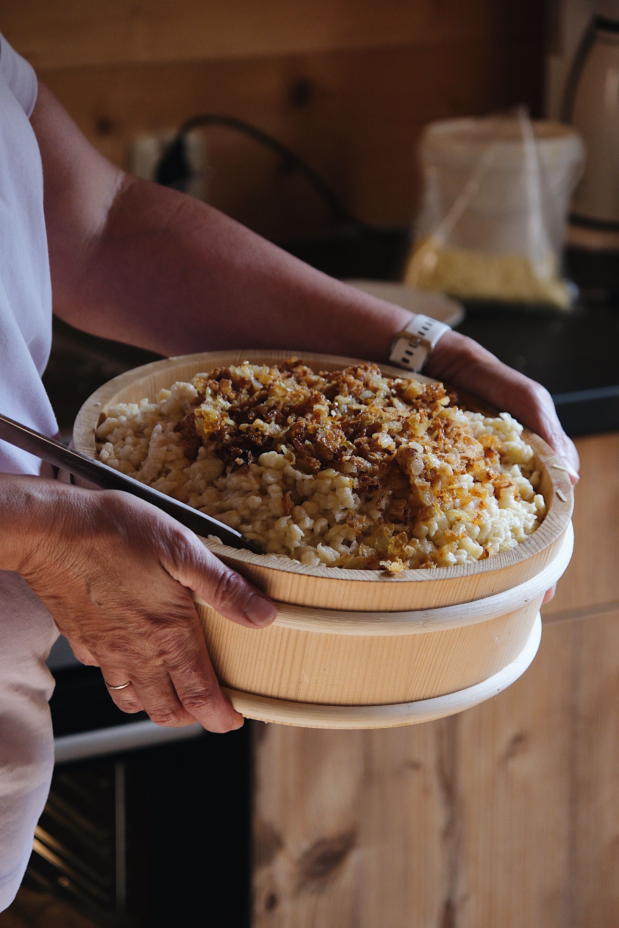 Una persona sosteniendo un cuenco de madera con comida, posiblemente arroz, y un aderezo.