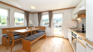 A modern kitchen with wooden cabinets, a built-in oven, and a dining area with a bench and chairs.