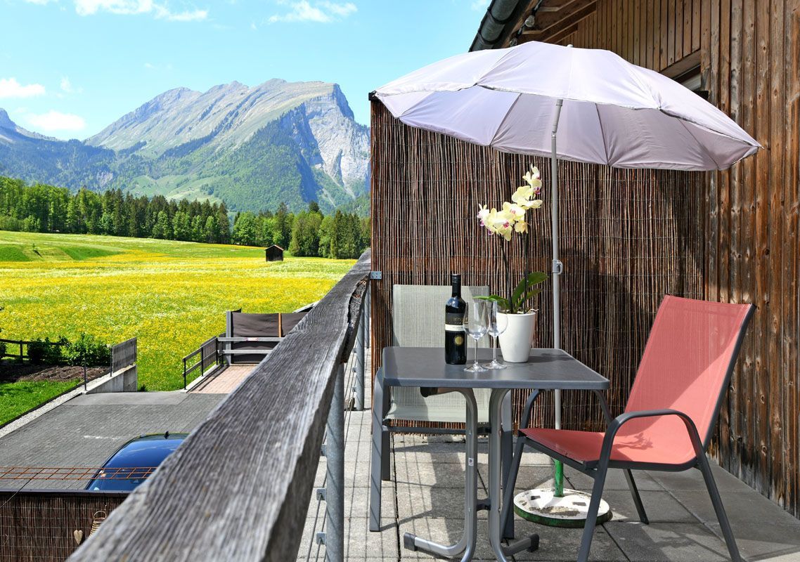 Un balcon avec une table, des chaises, une bouteille de vin et un parasol.