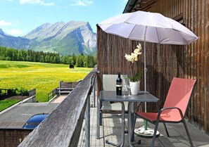 A balcony with a table, chairs, a bottle of wine, and an umbrella.