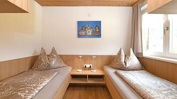 Quarto com duas camas, uma mesinha, um quadro na parede e uma janela com cortinas.