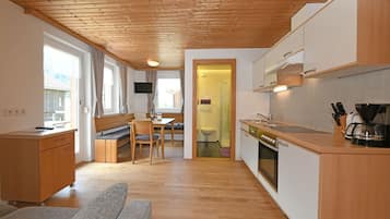 A compact kitchen with wooden cabinets, a dining area with a bench, and a visible bathroom.