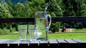 A wooden table with a glass pitcher and two glasses, set against a mountain backdrop.