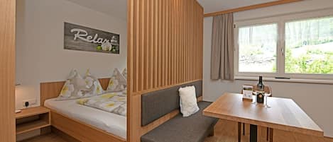 A compact room with a bed, a bench, a table, and a window with a view.