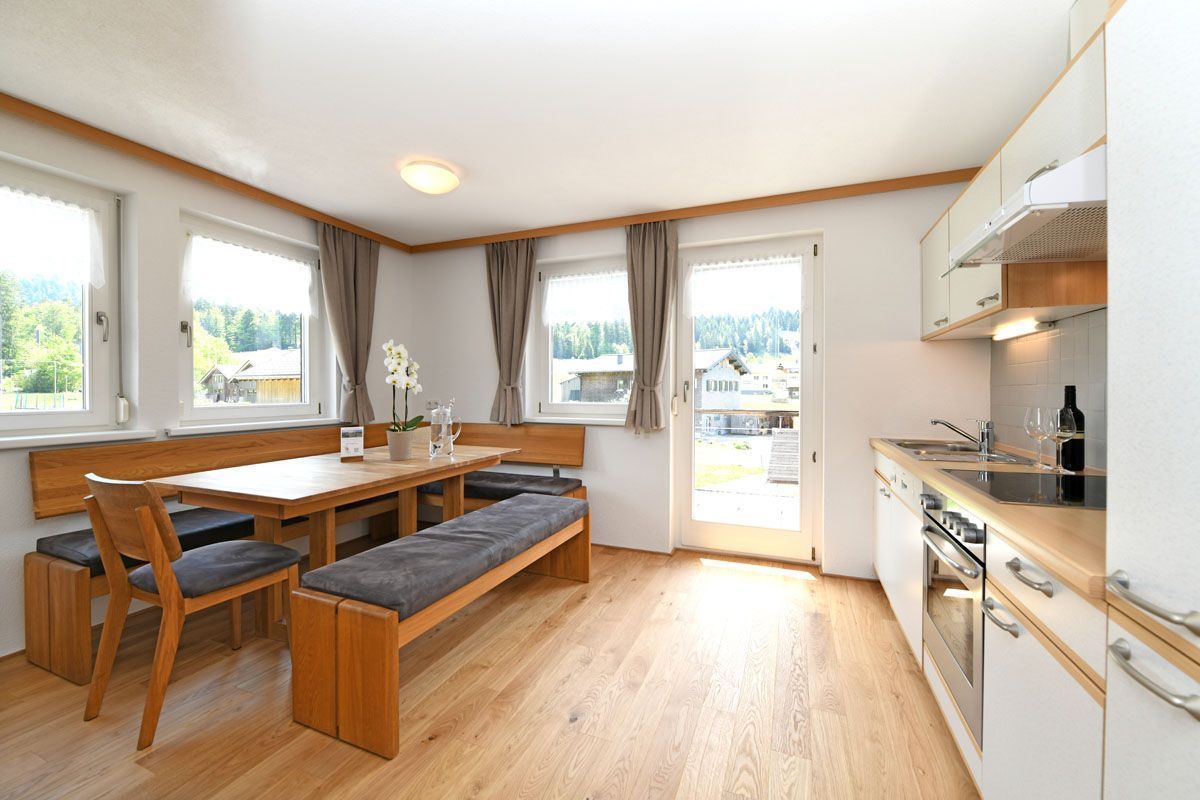 Eine moderne Küche mit Holzschränken, einem eingebauten Backofen und einem Essbereich mit einer Bank und Stühlen.
