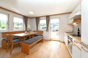 Una cocina moderna con armarios de madera, horno empotrado y comedor con banco y sillas.