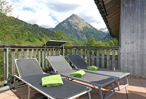 A balcony with two sun loungers, a wooden fence, and a mountain view.