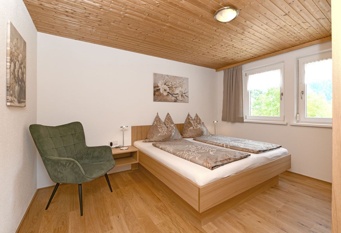 Une chambre avec un plafond en bois, un lit avec des oreillers, une chaise verte et une table de chevet.