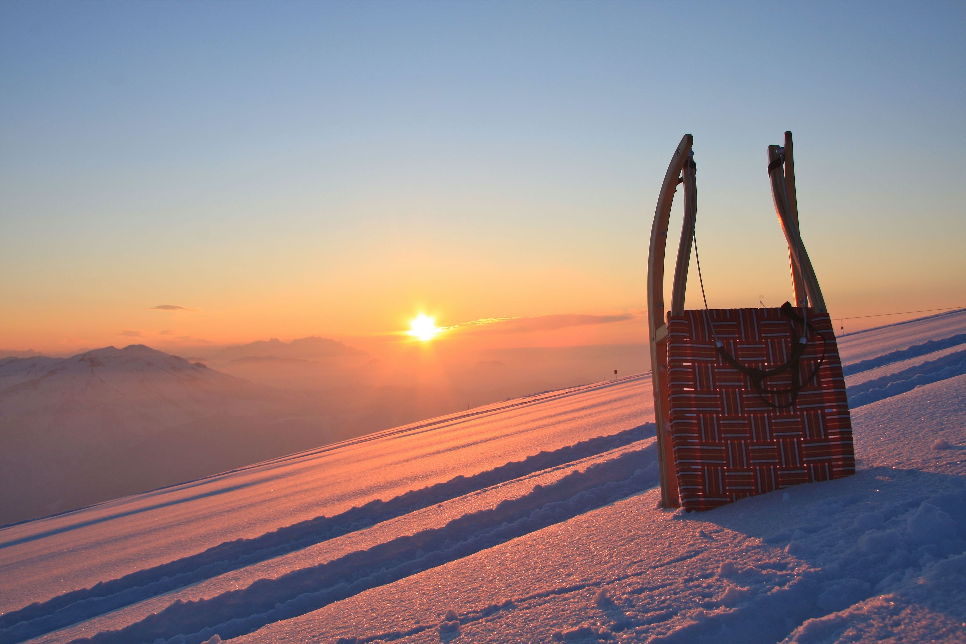 A patterned bag on a snowy slope with a sunset in the background.