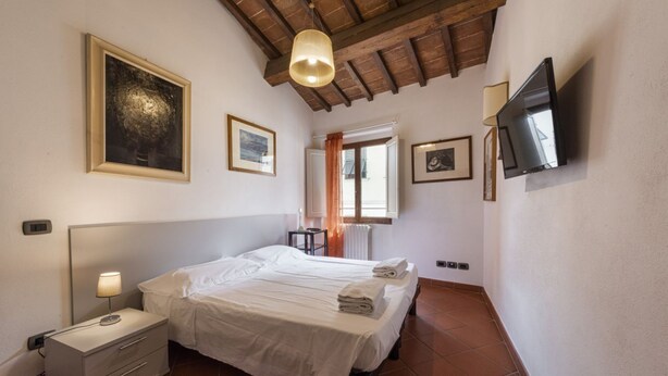 A bedroom with a bed, bedside table, lamp, and a TV mounted on the wall. - San Frediano House, beautiful apartment in Via Romana by Mmega (Firenze)
