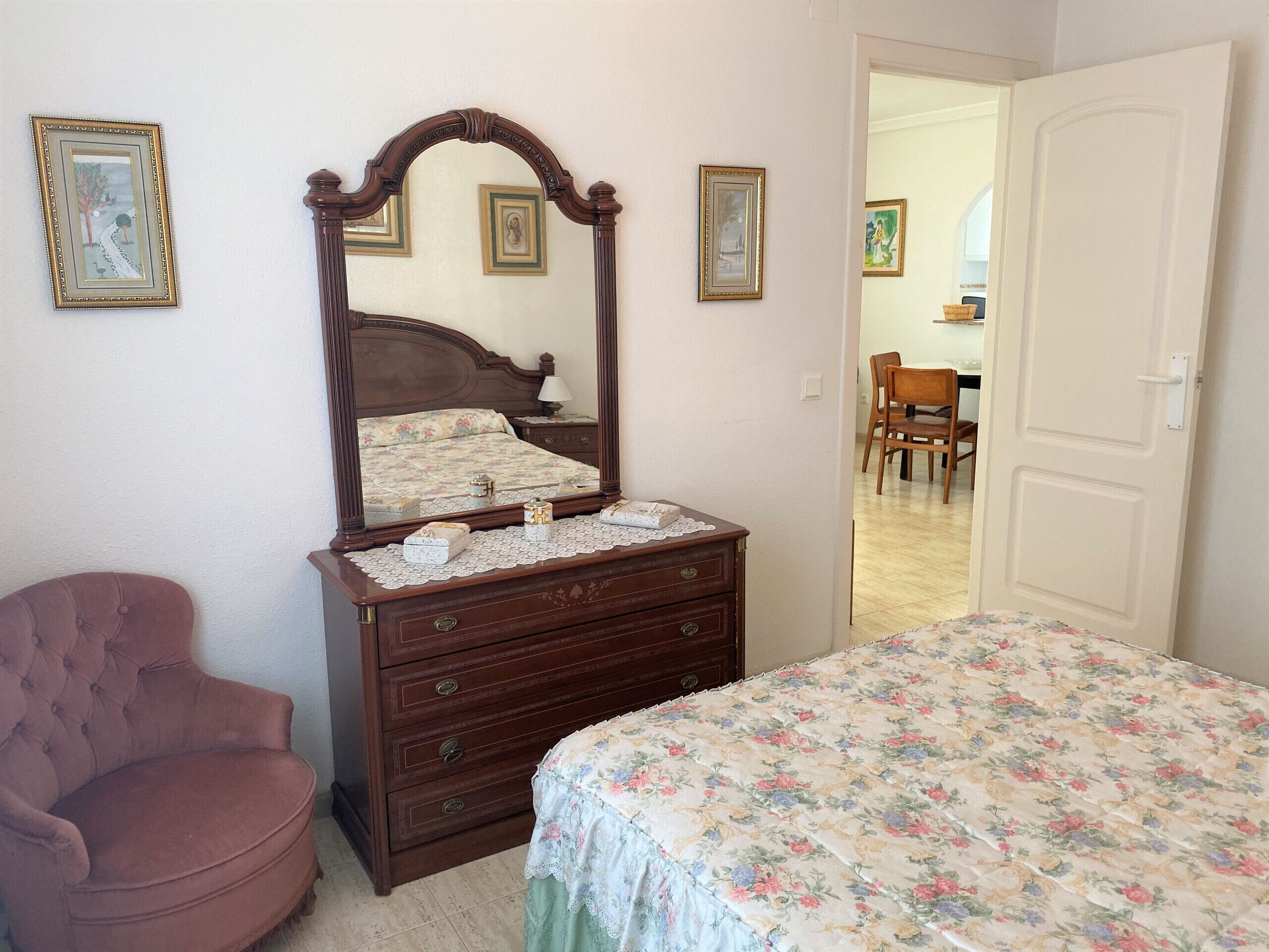 Een slaapkamer met een bed, een dressoir, een stoel en een spiegel.