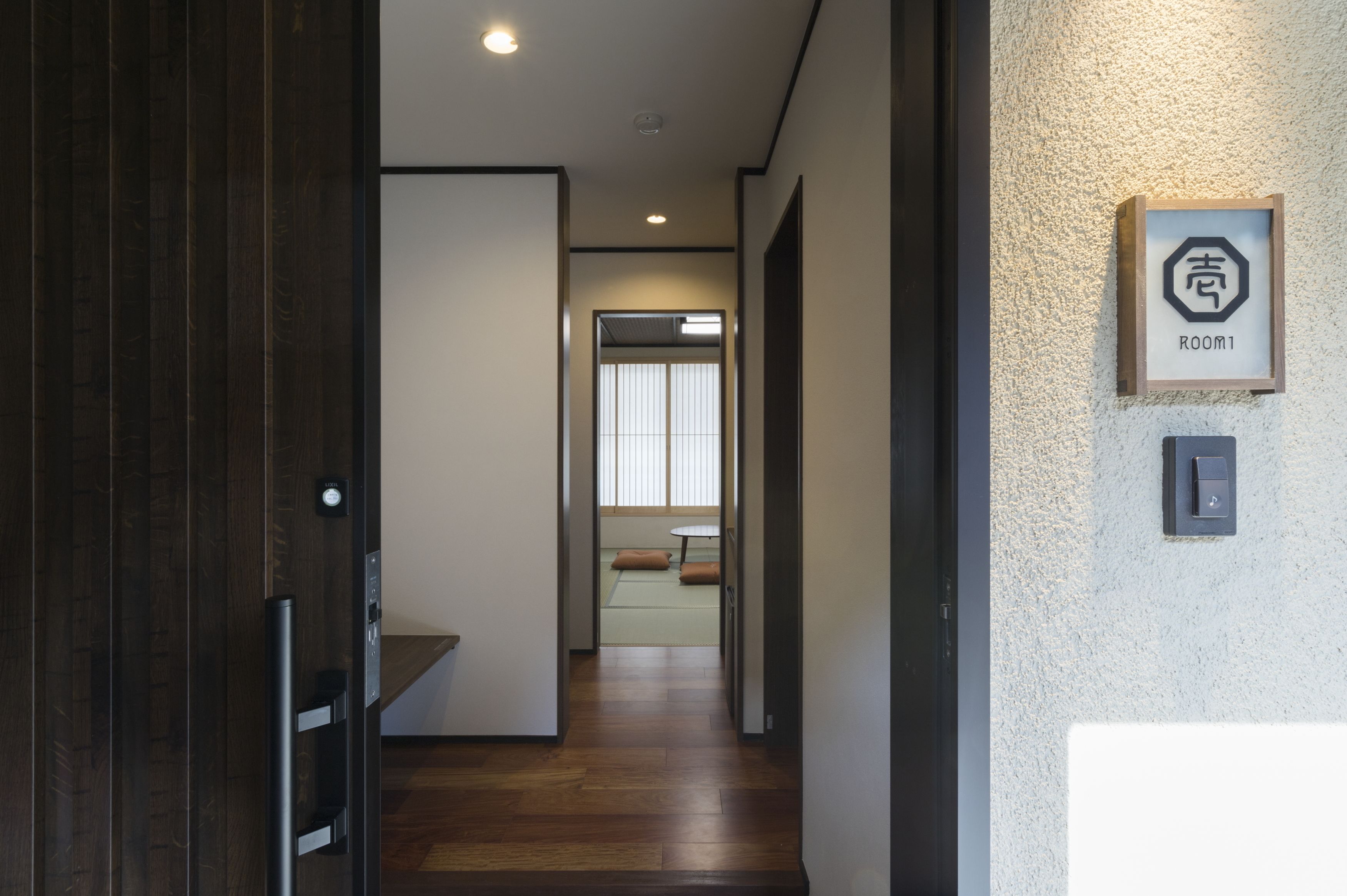 A hallway with wooden flooring, a door on the left, and a sign indicating Room 1 on the right.