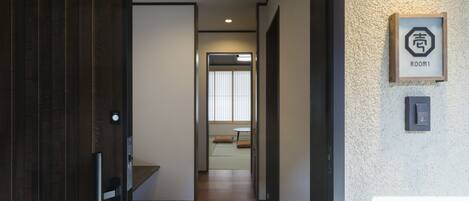 A hallway with wooden flooring, a door on the left, and a sign indicating Room 1 on the right.