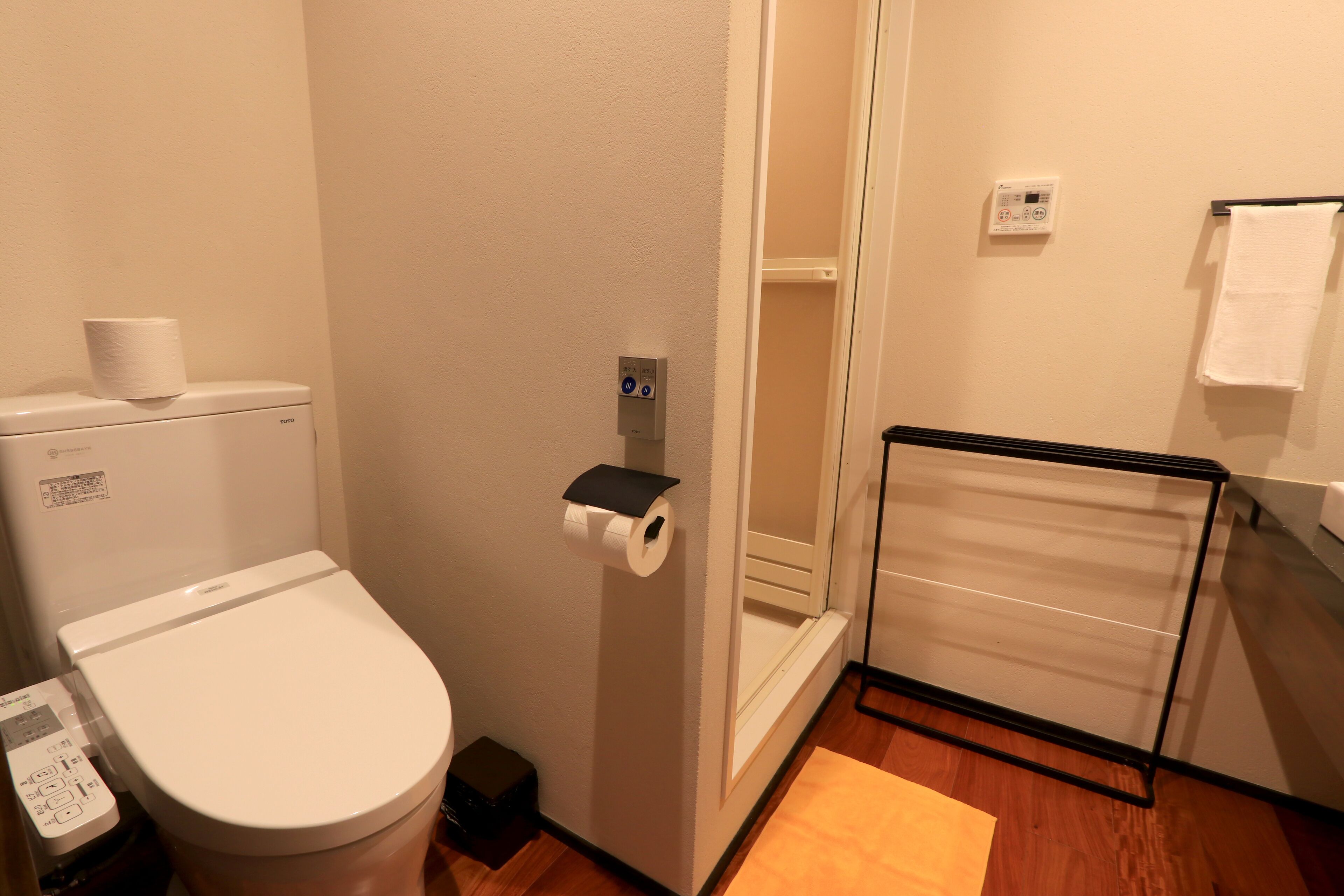 Een badkamer met een toilet, een papieren handdoekhouder, een handdoekrek en een houten vloer.