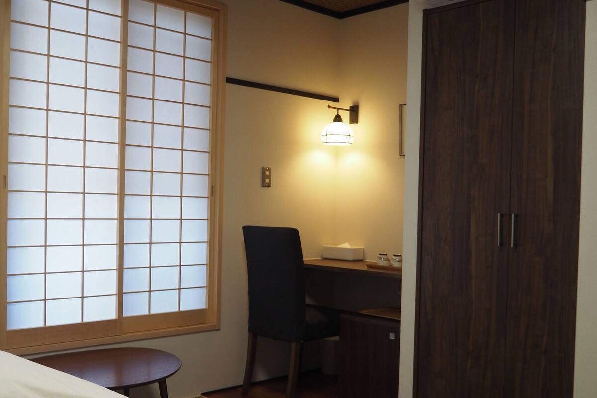 A room with a bed, a desk with a chair, a wardrobe, and a window with a view.