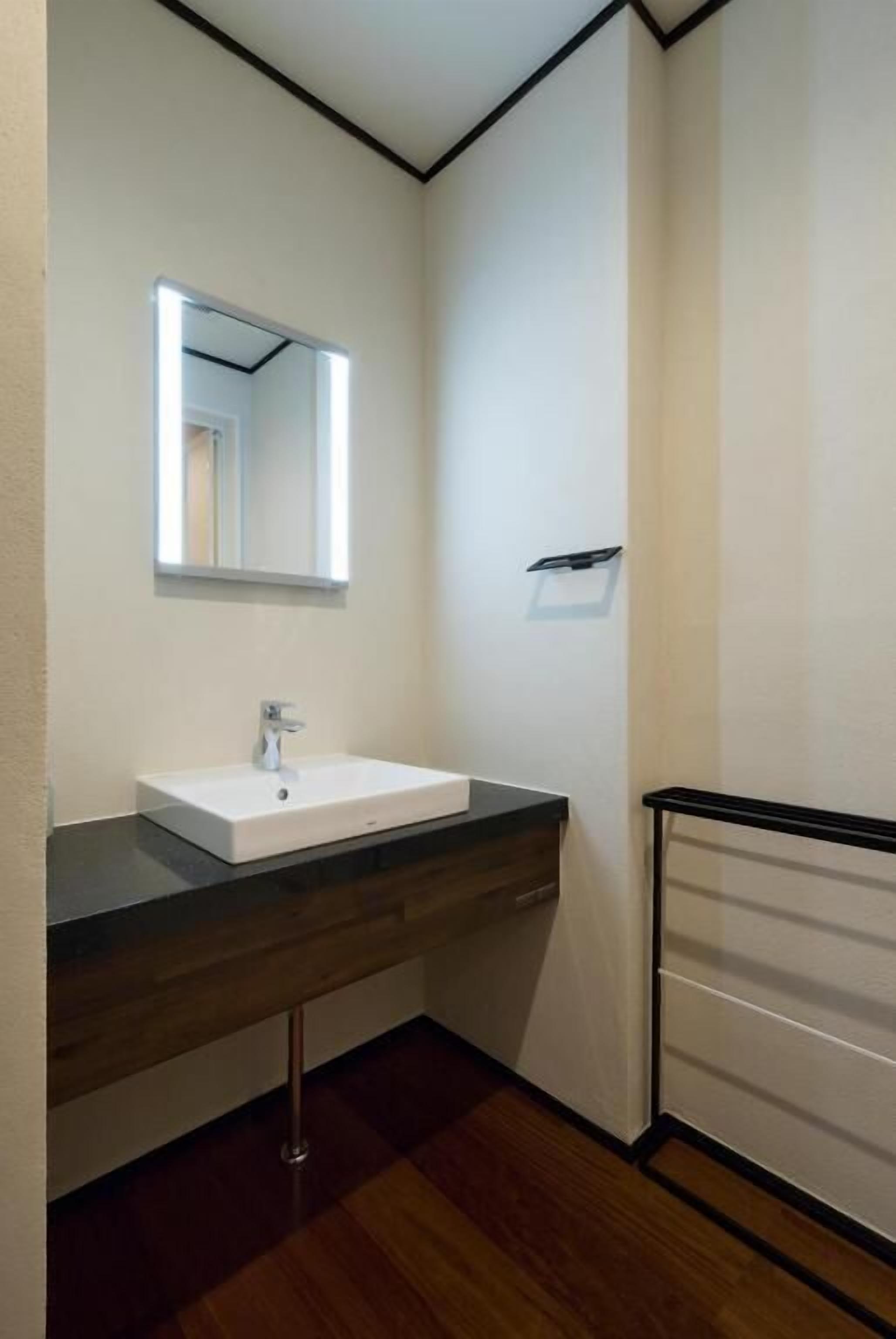 Un baño con lavamanos blanco, un espejo con iluminación integrada, un mueble de tocador de madera y una cabina de ducha con marco negro.