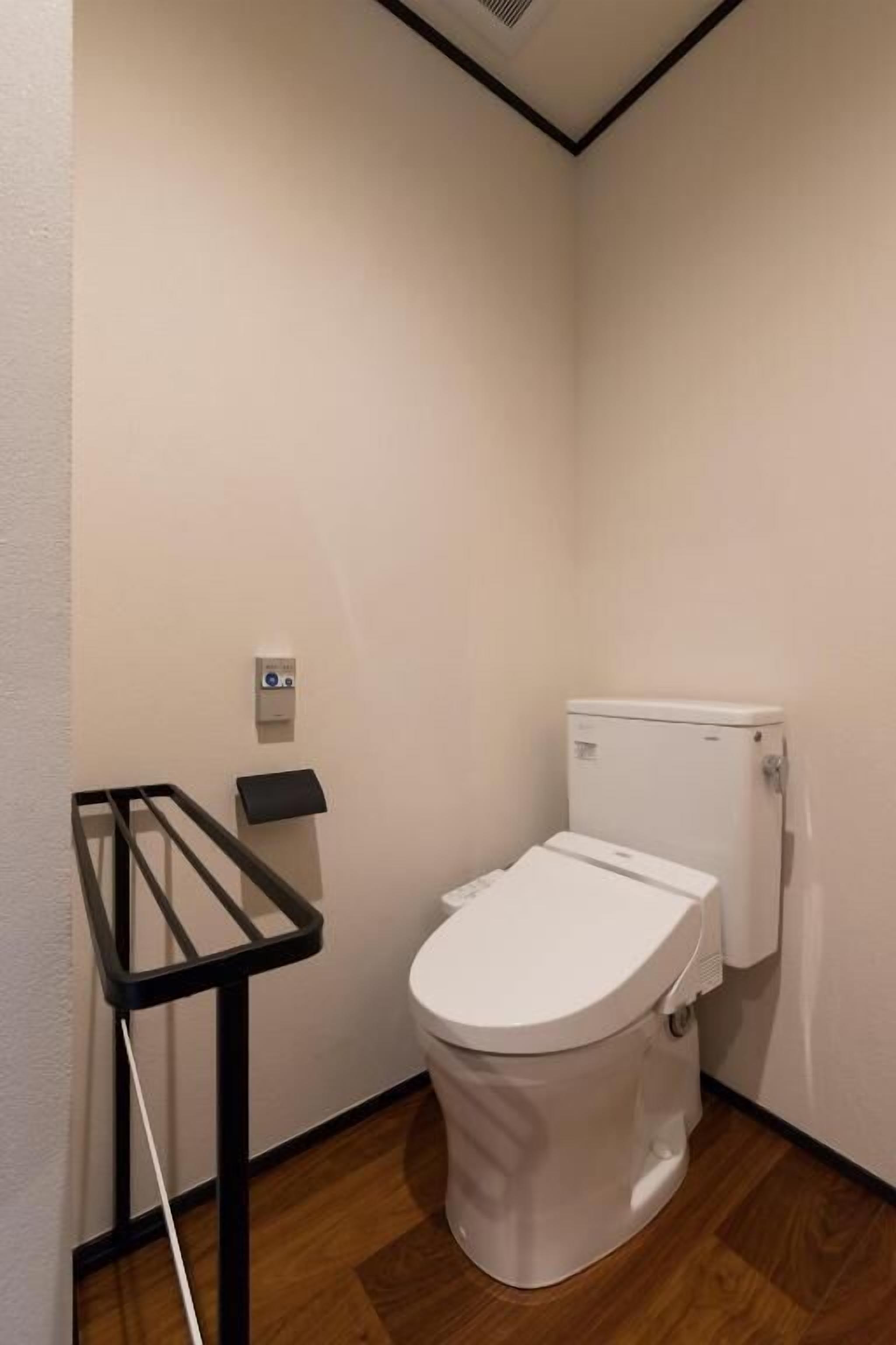Un baño pequeño y limpio con inodoro blanco, repisa metálica negra y suelo de madera.