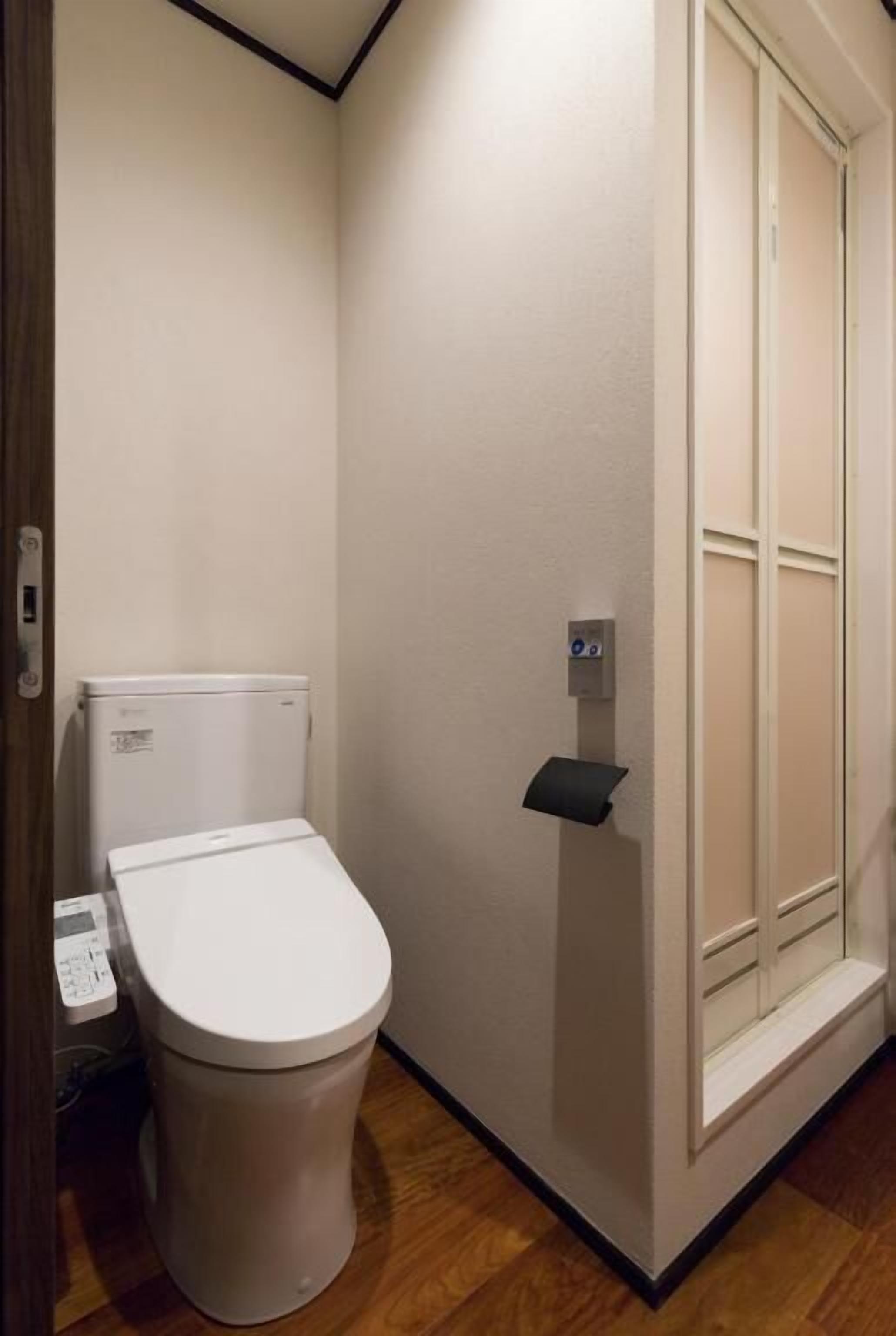 A small, clean bathroom with a toilet, a paper towel dispenser, and a window with blinds.