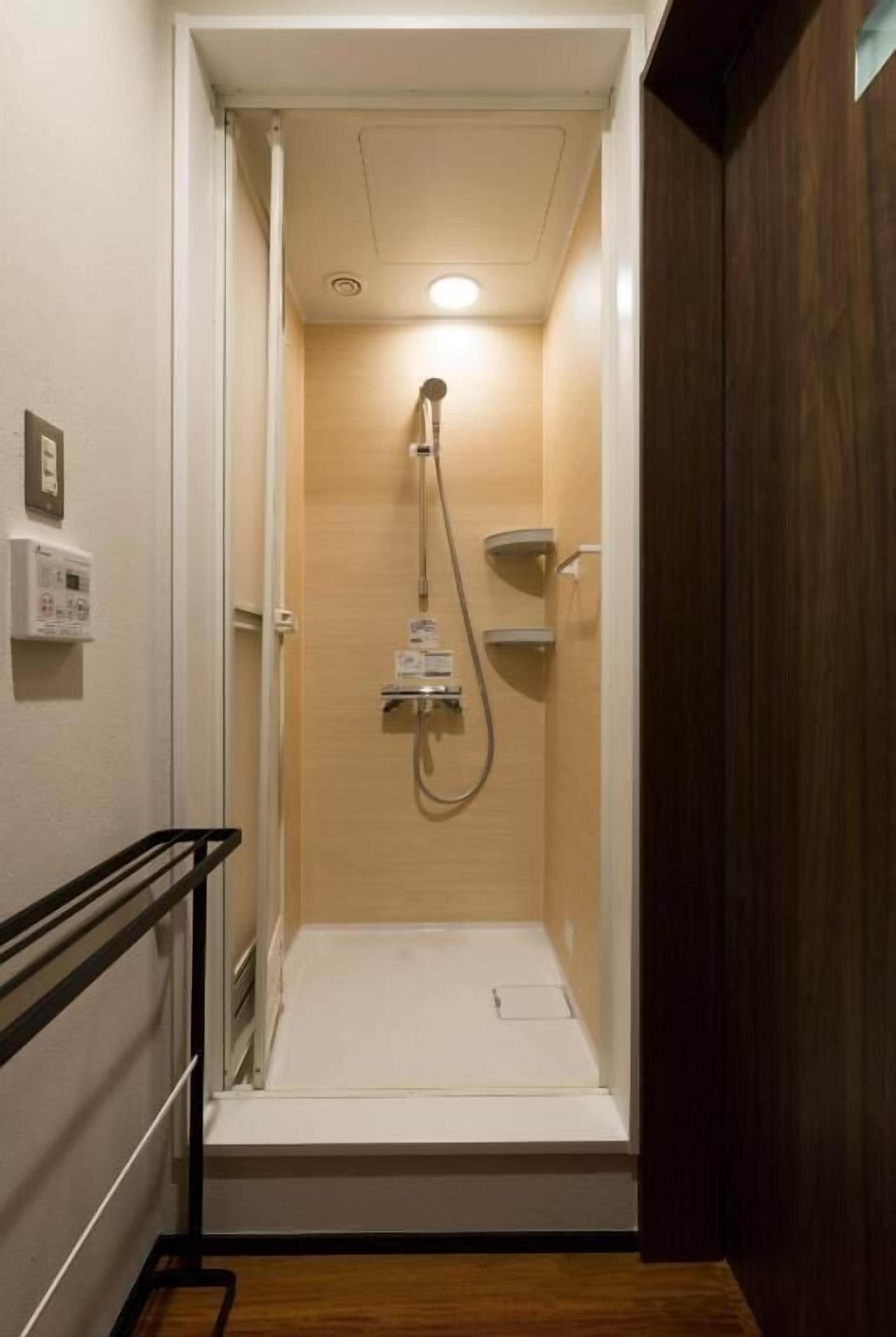 A small, enclosed shower area with a control panel and a handheld showerhead.