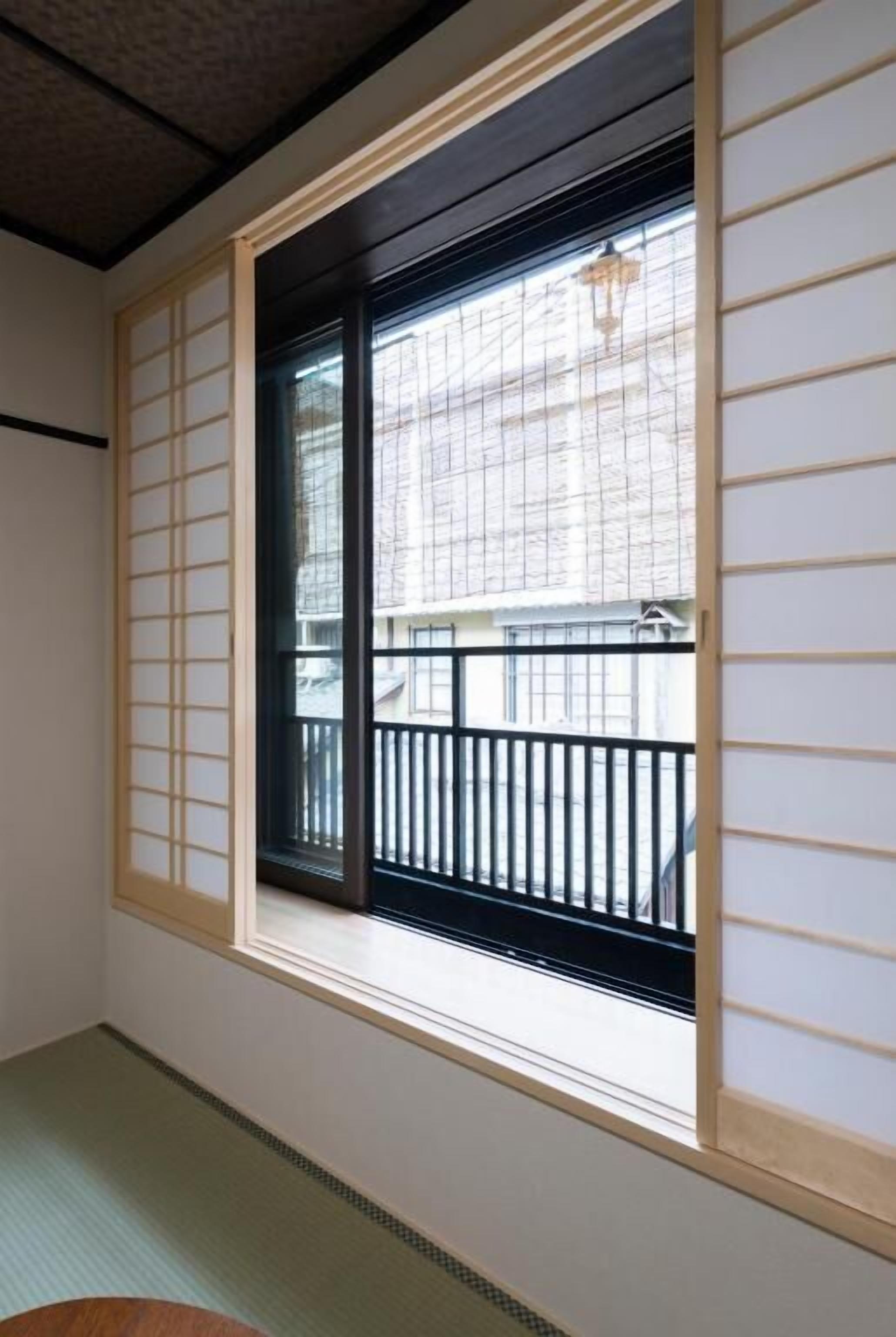 A room with tatami flooring, a sliding shoji screen, and a view of a balcony with a black railing.