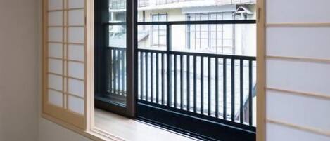 A room with tatami flooring, a sliding shoji screen, and a view of a balcony with a black railing.