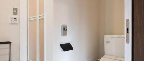 A bathroom with a toilet, a window, and a wall-mounted control panel.