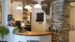 A reception area with a stone wall, wooden counter, and hanging lights. - Das Gästehaus in Valwig (Valwig)